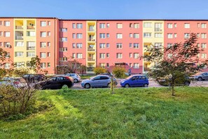 En flereetagers boligbygning med altaner, parkerede biler og en grøn græsplæne foran.