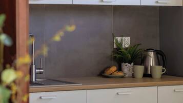 A modern kitchen with white cabinets, a wooden countertop, a coffee maker, and a potted plant.