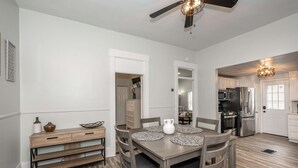 A dining area with a wooden table, chairs, and a bench. There is a ceiling fan, a light fixture, and a kitchen visible in the background. - The Washington Cottage - 6ppl (Harrison)