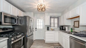 A modern kitchen with stainless steel appliances, white cabinetry, and a wooden floor. - The Washington Cottage - 6ppl (Harrison)