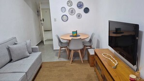 En hyggelig stue med en grå sofa, et rundt spisebord med stole, et fjernsyn og en væg pyntet med dekorative tallerkener.
