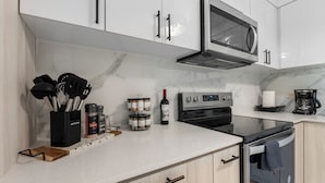 A modern kitchen with white cabinets, a stainless steel microwave, an oven, and a coffee maker. - Oceanview Luxury Villa Near El Yunque w/Hot Tub (Las Coles)