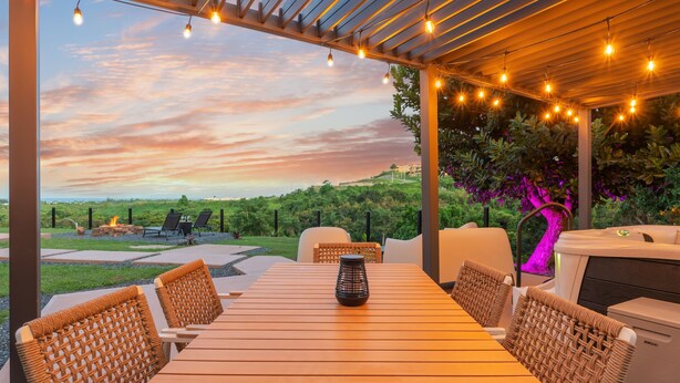 An outdoor patio with a wooden table and wicker chairs, overlooking a scenic landscape with a fire pit and grill. - Oceanview Luxury Villa Near El Yunque w/Hot Tub (Las Coles)