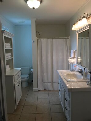 A bathroom with a toilet, a shower curtain, a sink with a mirror, and a towel rack.