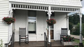 En vit byggnad med en veranda, två stolar och hängande blomkrukor.