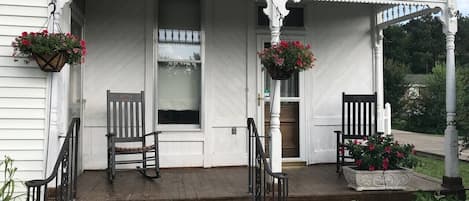 A white building with a porch, two chairs, and hanging flower baskets.
