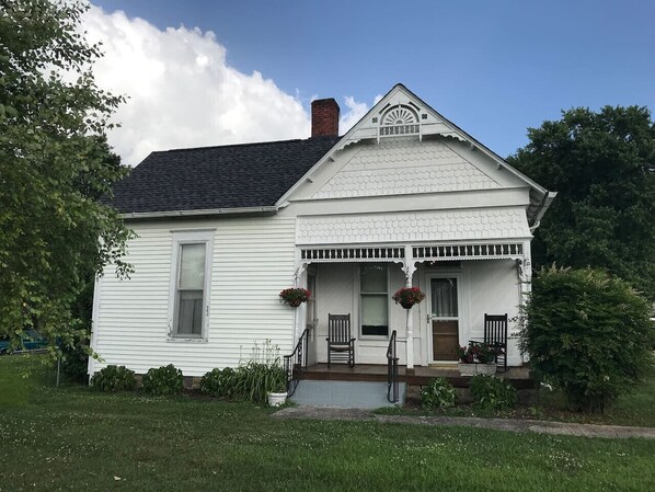 A white two-story house with a front porch, a chimney, and a small garden area.