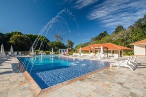 A swimming pool with a water fountain, lounge chairs, and a covered area with a red roof.