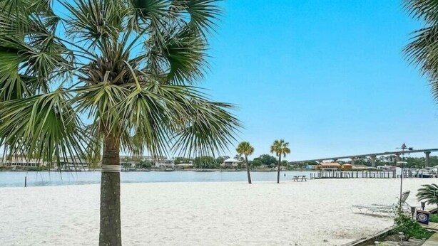 Ein Strand mit einer Holzpromenade, Palmen und einem klaren, blauen Himmel.