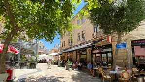 Ein Straßencafé mit Tischen und Stühlen, umgeben von Gebäuden und Bäumen.