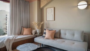 Ein modernes Wohnzimmer mit einem grauen Sofa, einem runden Couchtisch und einem Fenster mit Vorhängen.