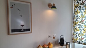 Et moderne køkken med et træbord, en sort stol, et indramet kunstværk, en vægmonteret lampe og en dekorativ plante.