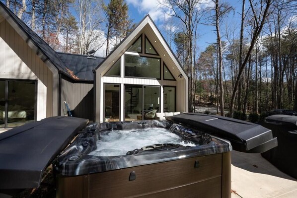 Una casa moderna con jacuzzi, grandes ventanales y un fondo boscoso.