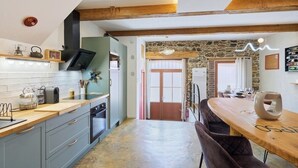 Une cuisine moderne avec des meubles gris, un plan de travail en bois et un mur en pierre. On y trouve également un coin repas avec une table et des chaises en bois.