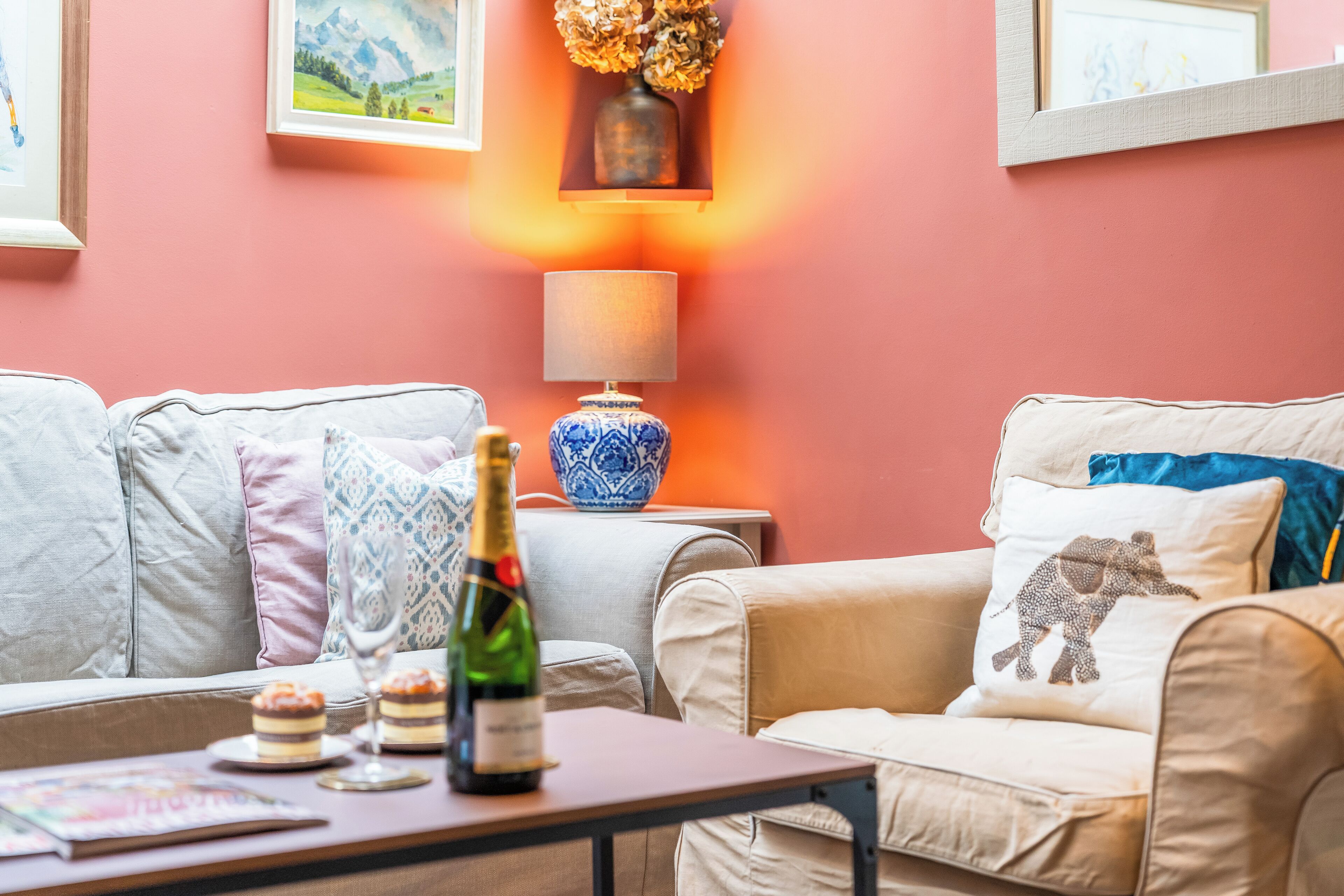 Un salon chaleureux avec un canapé, une petite table sur laquelle se trouvent une bouteille et des verres, et une lampe.