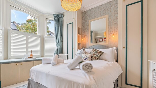 Un dormitorio con una cama grande, una ventana con cortinas, una mesita de noche y un espejo instalado en la pared.