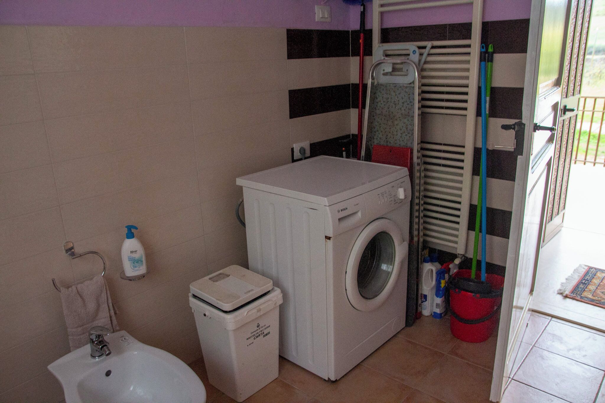 A compact laundry area with a washing machine, a small sink, and a trash bin.