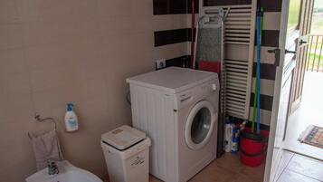 A compact laundry area with a washing machine, a small sink, and a trash bin.