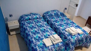 Una habitación con dos camas, cada una con una colcha estampada y toallas dobladas. Hay una mesita de noche con una lámpara y una pequeña mesa con un teléfono.