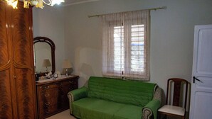 Una habitación con un sofá verde, un armario de madera, una silla, un espejo y una ventana con cortinas.