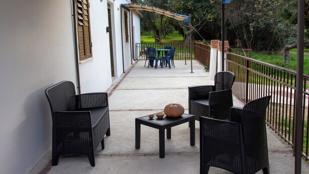 Un patio al aire libre con mobiliario de mimbre negro, una mesa con una calabaza y un bol, y un área cubierta con una pérgola.