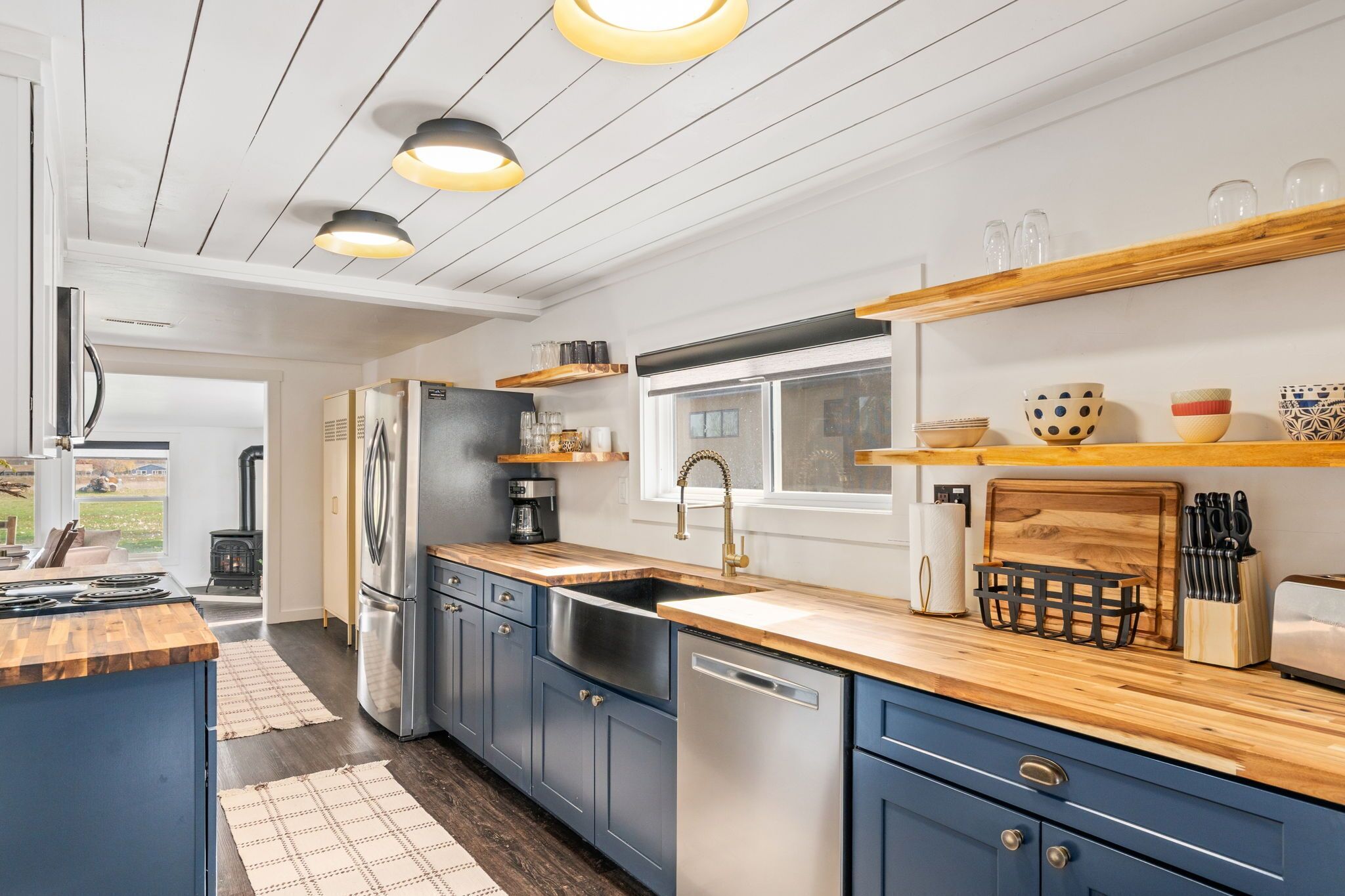 A modern kitchen with blue cabinets, stainless steel appliances, wooden countertops, and pendant lighting.