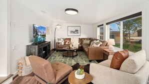 A modern living room with a sectional sofa, a television, a fireplace, and a large window offering a view of the outdoors. - Sunset Haven Dog-friendly Home Near Trails/lake (Fort Collins)