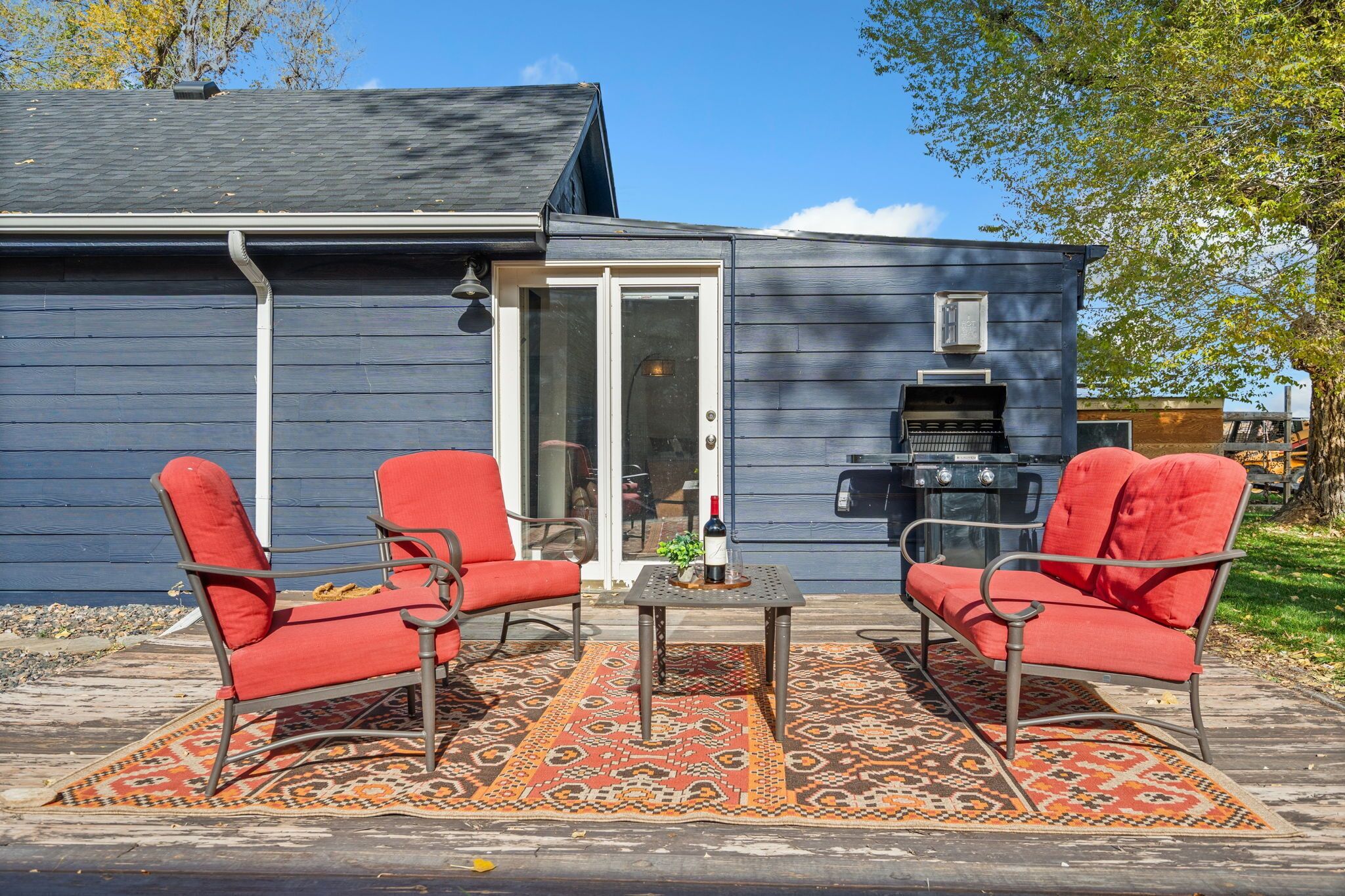 Une terrasse avec deux chaises rouges et une table, un barbecue et une porte-fenêtre coulissante.
