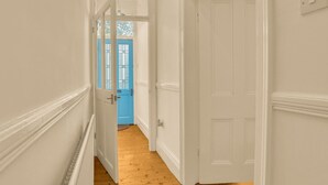 Un couloir aux murs blancs, doté d’un plancher en bois et d’une porte bleue au fond.