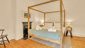Un lit à baldaquin avec une couvre-lit bleue, deux tables de chevet avec des lampes, une cheminée et un tableau encadré au mur.