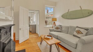 Un salon avec un canapé gris, une table basse en bois, une cheminée et une vue sur un bâtiment en briques, visible à travers une fenêtre.