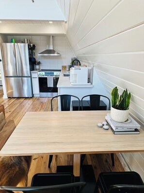 A modern kitchen with stainless steel appliances, a white countertop, and a dining area with a wooden table and chairs.