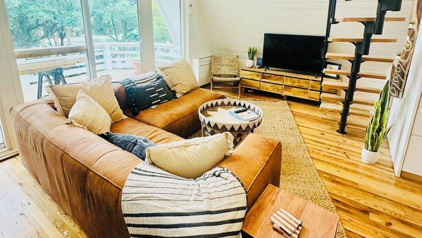 A spacious living room with a large sectional sofa, a flat-screen TV, wooden flooring, and a staircase.
