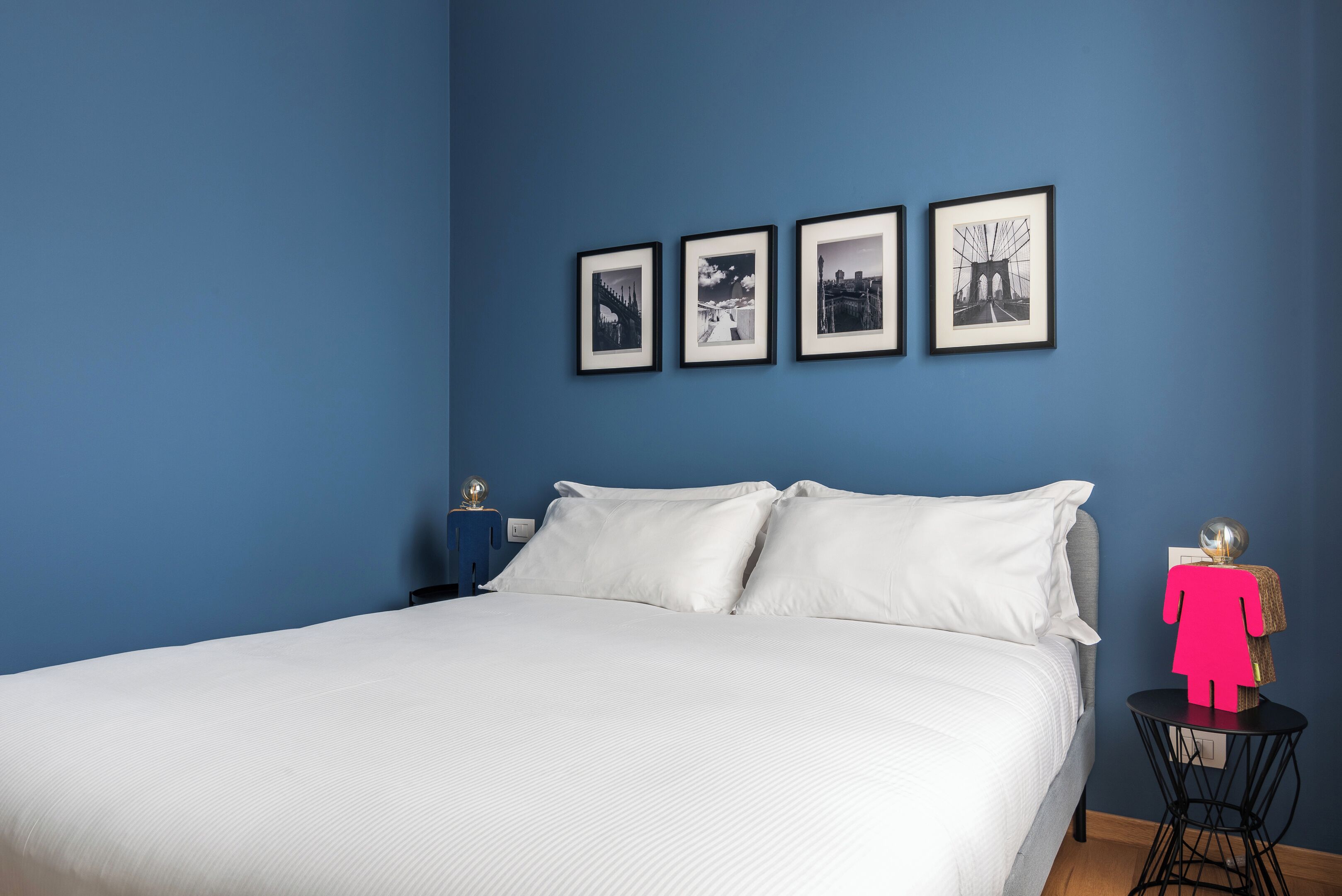 A bedroom with a bed, white bedding, a blue wall, and four framed pictures.