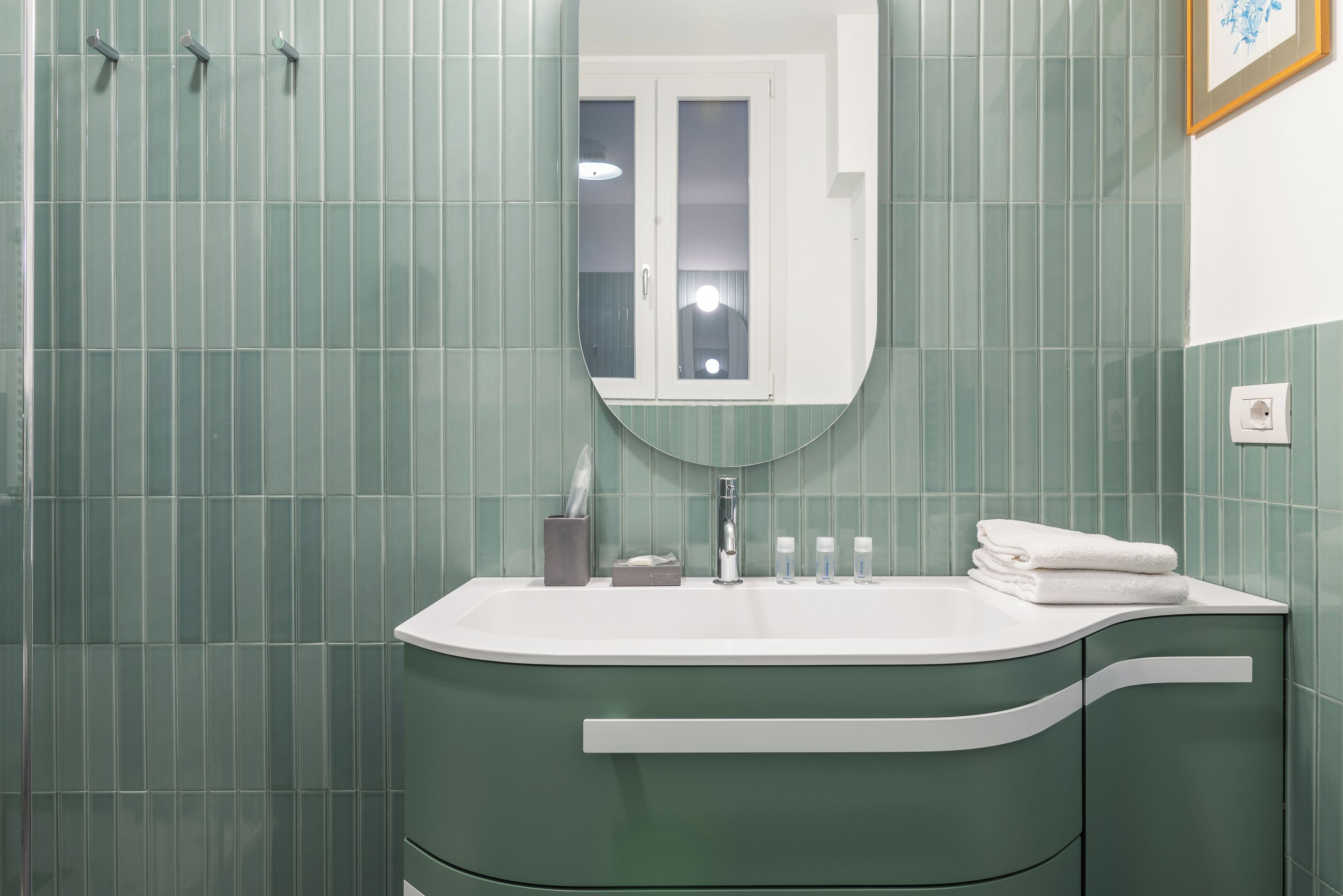 A bathroom with a green tiled wall, a white sink, and a mirror above it.