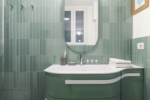Ein Badezimmer mit grüner Fliesenwand, einem weißen Waschbecken und einem Spiegel darüber.