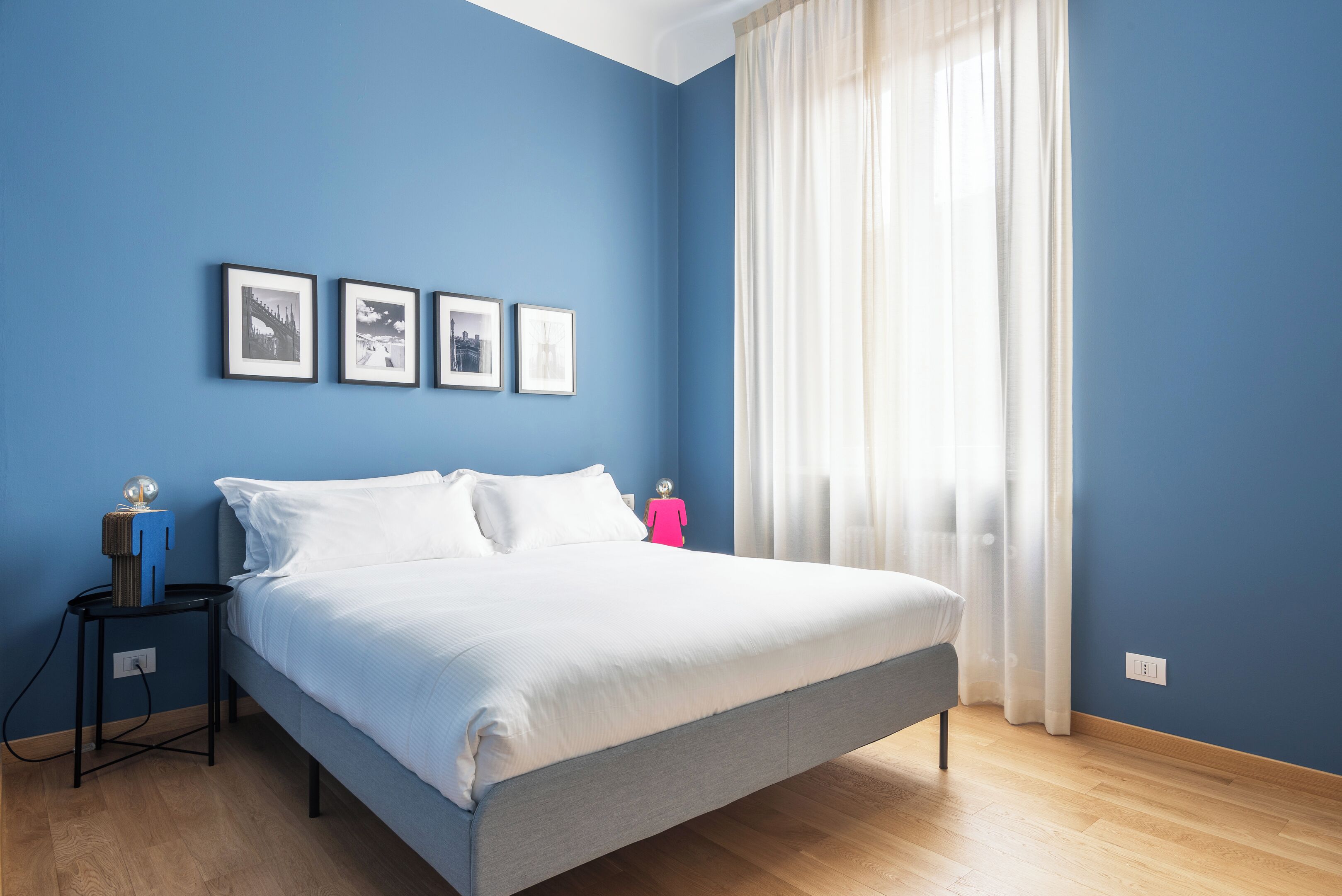 A bedroom with a bed, a nightstand, a lamp, and a window with curtains.