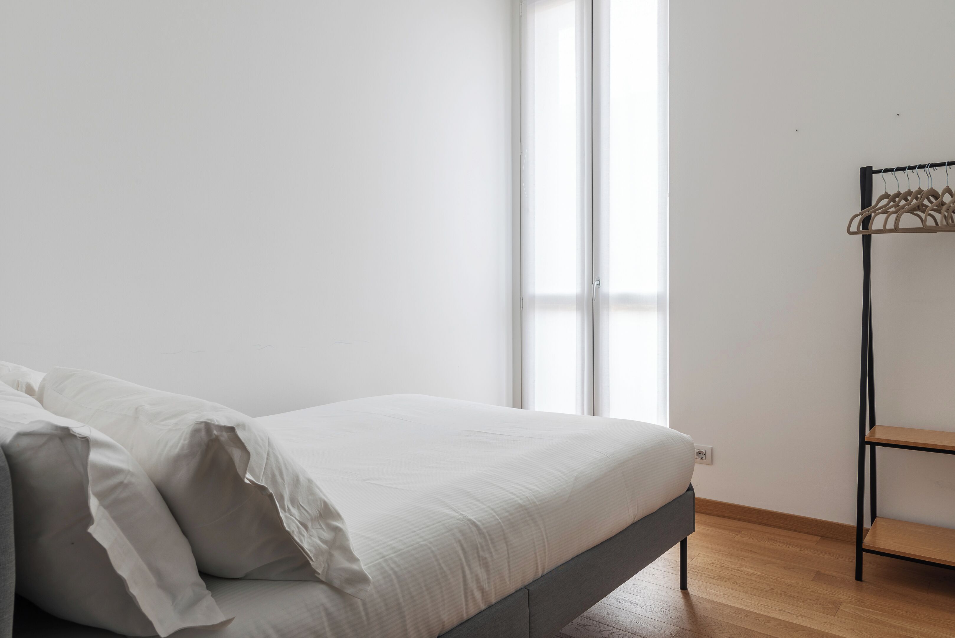 A minimalist bedroom with a bed, a window, and a wooden floor.