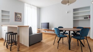 Una sala de estar moderna con una mesa de comedor de madera, sillas azules, un sofá gris y un televisor.