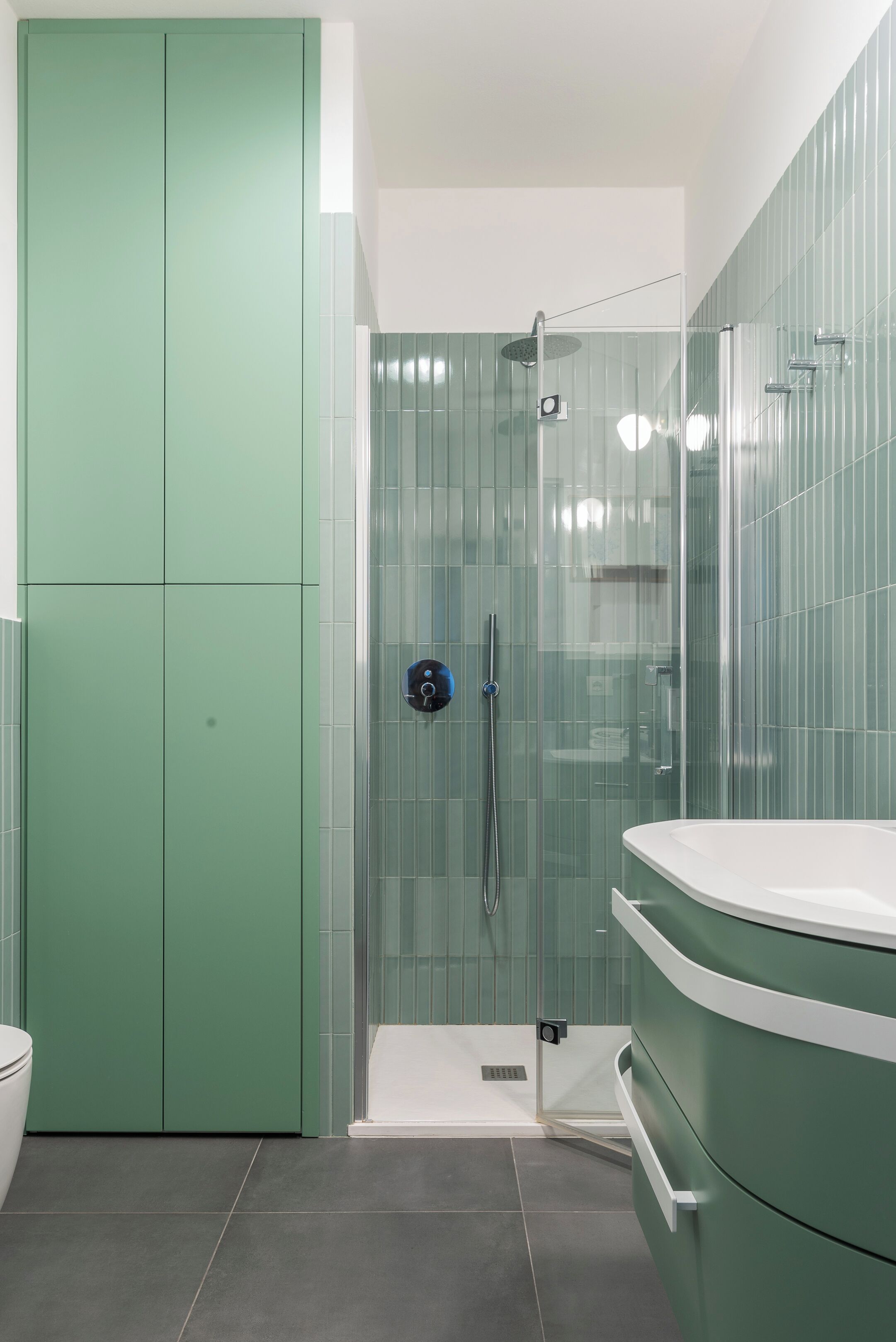 Un bagno moderno con doccia vetrata, un mobile lavabo verde e un water bianco.