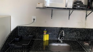 A kitchen with a black countertop, a stainless steel sink, a microwave, a blender, and a bottle of dish soap.