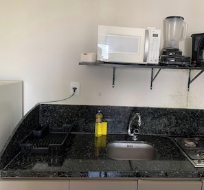 A kitchen with a black countertop, a stainless steel sink, a microwave, a blender, and a bottle of dish soap.