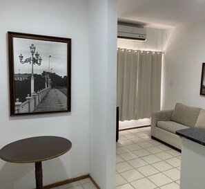 A living room with a sofa, a table, a framed picture, and a window with curtains.