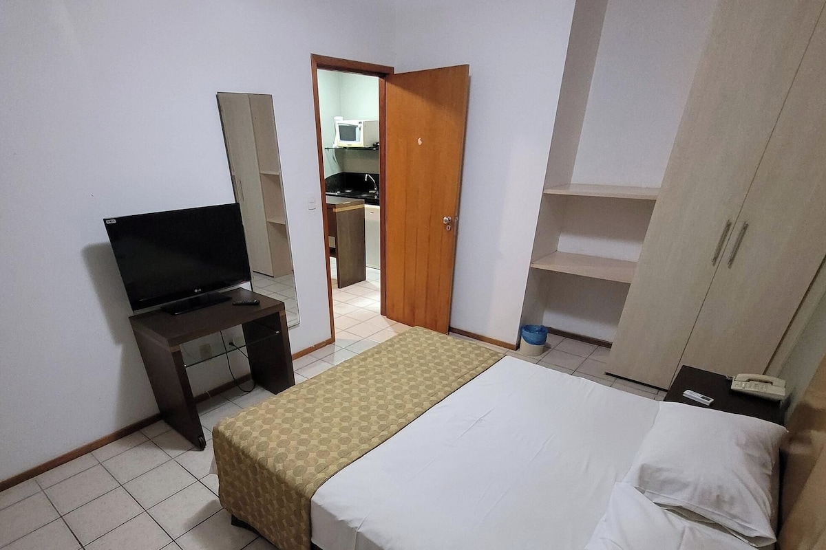 A hotel room with a bed, a TV on a stand, a wardrobe, and a door leading to a bathroom.