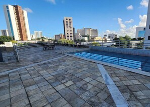 A rooftop terrace with a swimming pool, stone flooring, and a view of the city skyline.