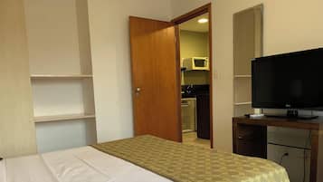 Un dormitorio con una cama, televisión, armario y una puerta que da a la cocina.