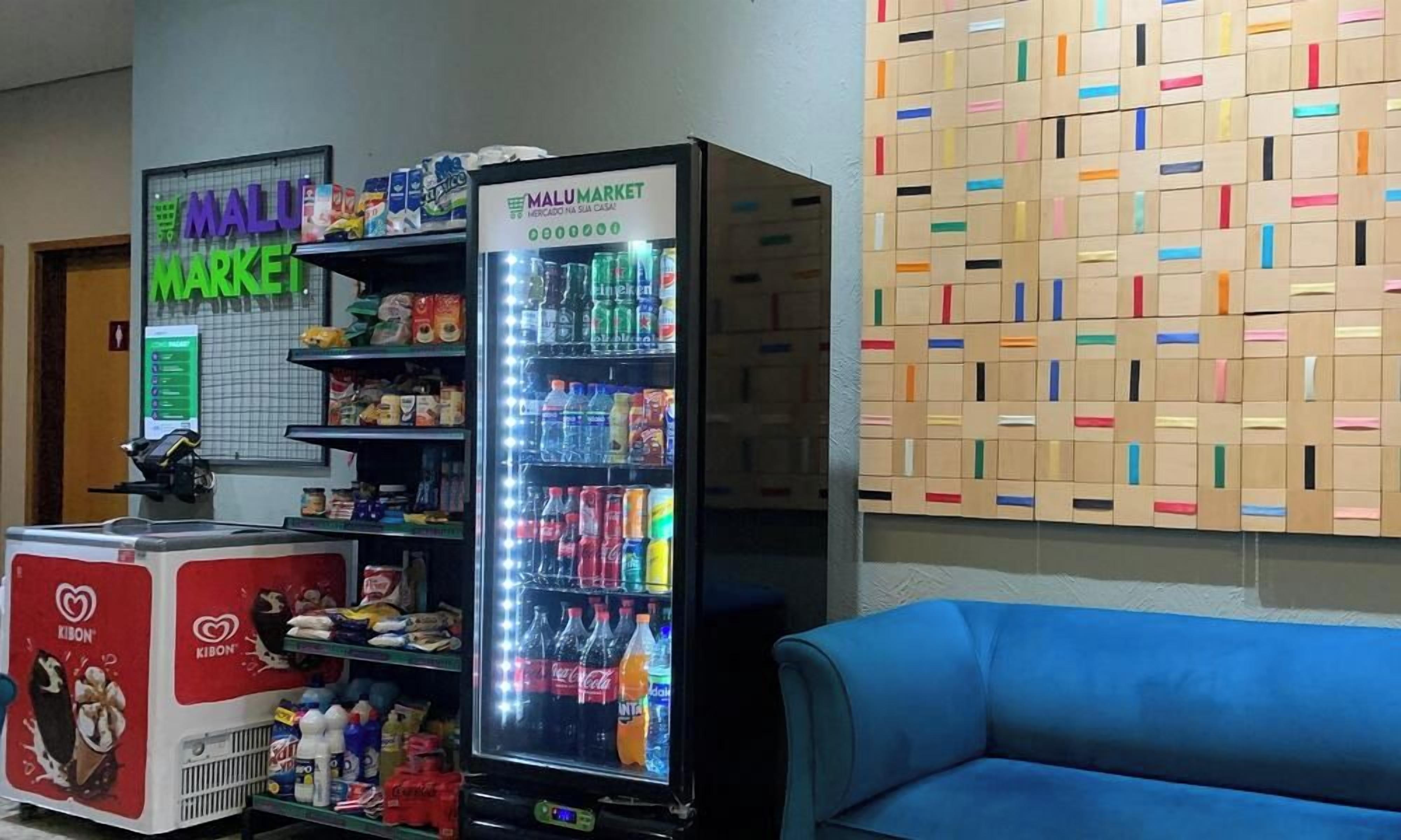 A vending machine with a variety of beverages and snacks, a refrigerator with ice cream, and a wall with colorful boxes.