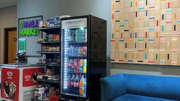 A vending machine with a variety of beverages and snacks, a refrigerator with ice cream, and a wall with colorful boxes.