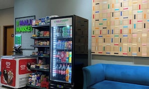 A vending machine with a variety of beverages and snacks, a refrigerator with ice cream, and a wall with colorful boxes.