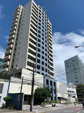 A tall, modern building with a grid-like facade, multiple balconies, and a clear sky.